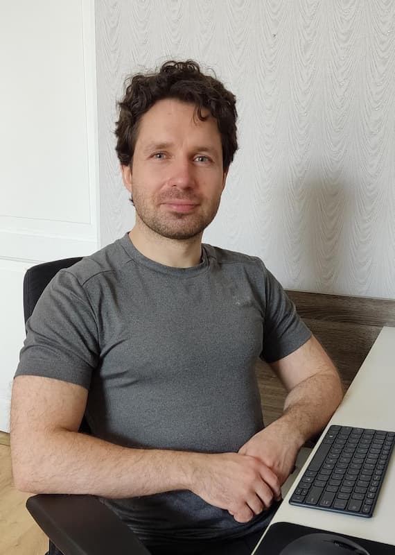 Anton Ždanov sitting in front of a laptop and smiling.